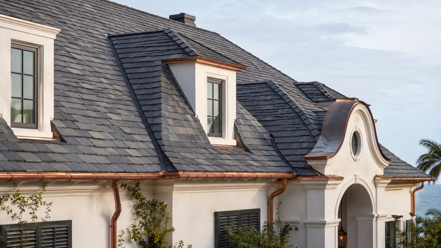 A close-up view of a luxury white home exterior featuring dark grey slate roof shingles and copper gutters.